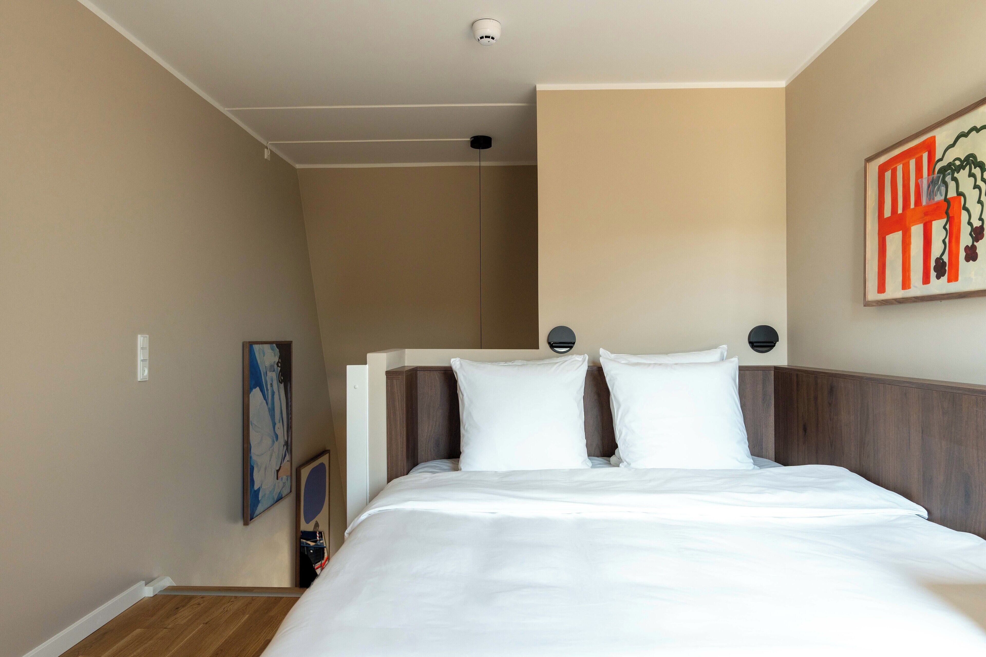 A hotel room with a bed, a wall-mounted artwork, and a ceiling light.