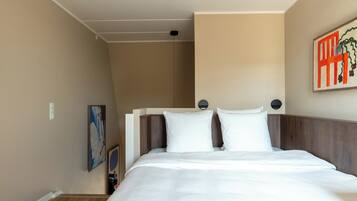 A hotel room with a bed, a wall-mounted artwork, and a ceiling light.