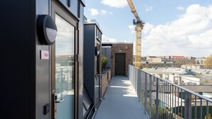 A narrow balcony with a view of a construction crane, a brick building, and a clear sky.