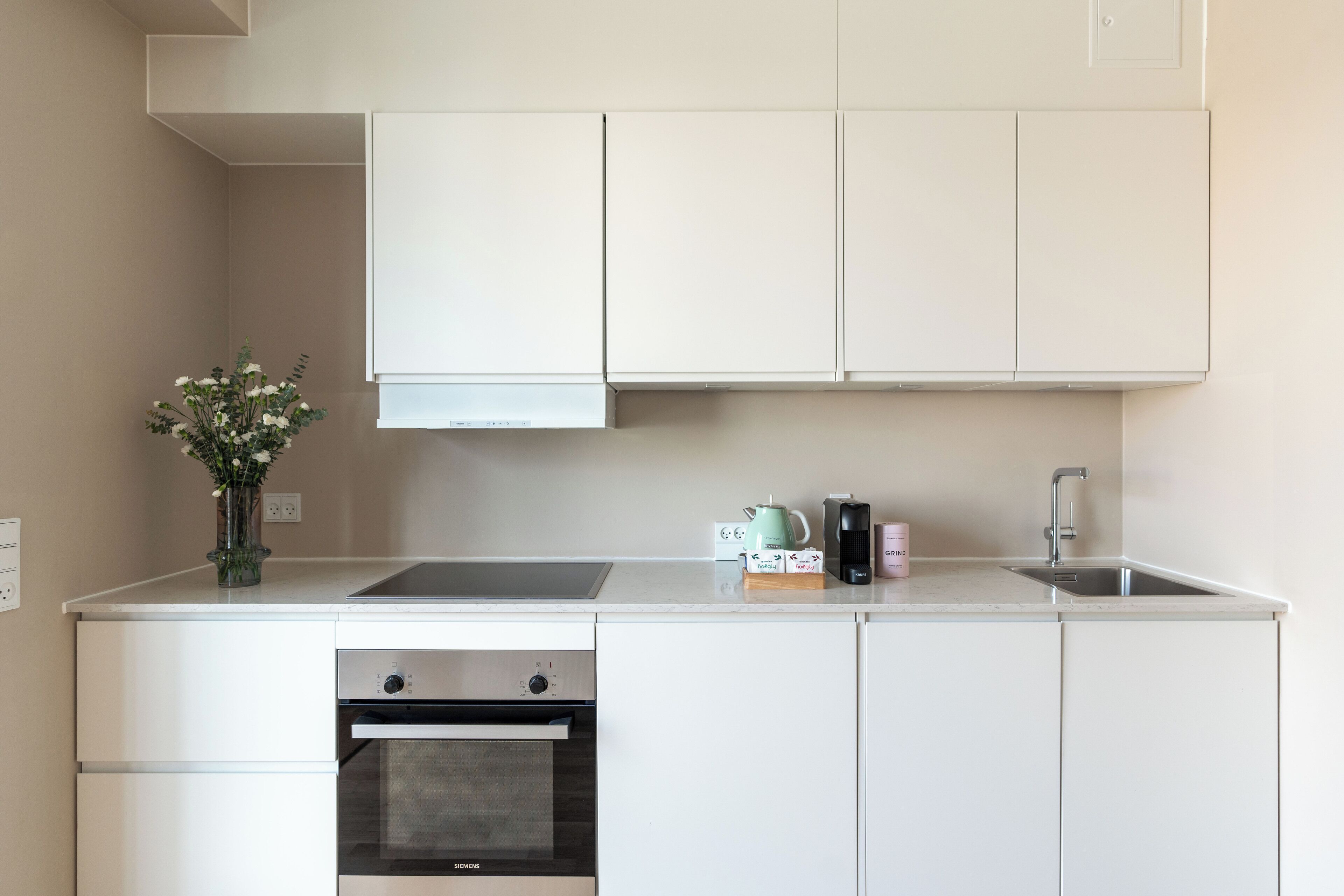 A modern kitchen with white cabinetry, a built-in oven, a sink, and a vase with flowers on the countertop.