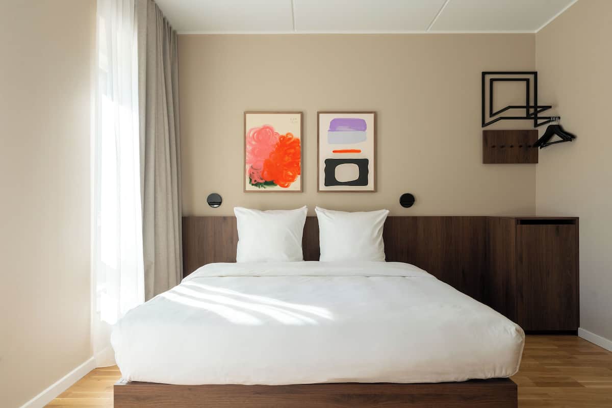 Una habitación de hotel moderna con una cama grande, cabecera de madera y dos cuadros enmarcados en la pared.