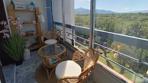 Un balcón con mobiliario de mimbre, una mesa de vidrio y vistas a un paisaje montañoso.