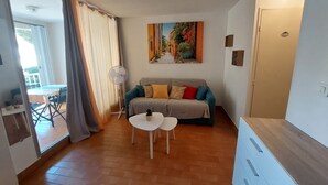 Una sala de estar con un sofá, una mesita, un ventilador y un cuadro en la pared.
