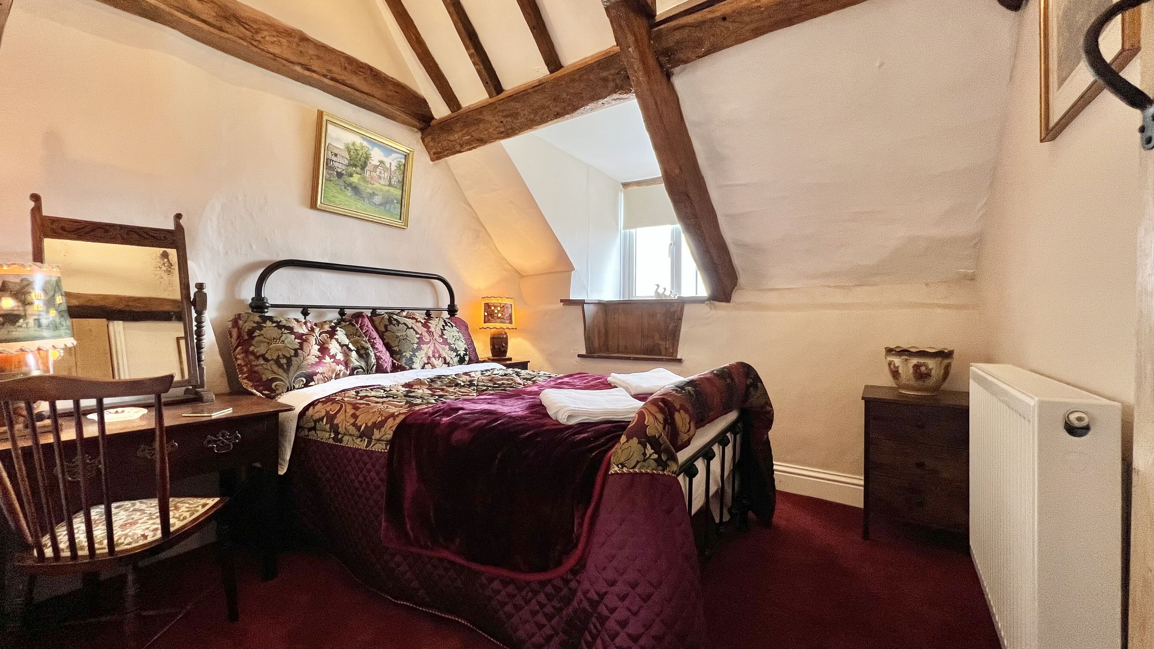 Ein Schlafzimmer mit Bett, Stuhl, Nachttisch, Lampe und einem Bild an der Wand.