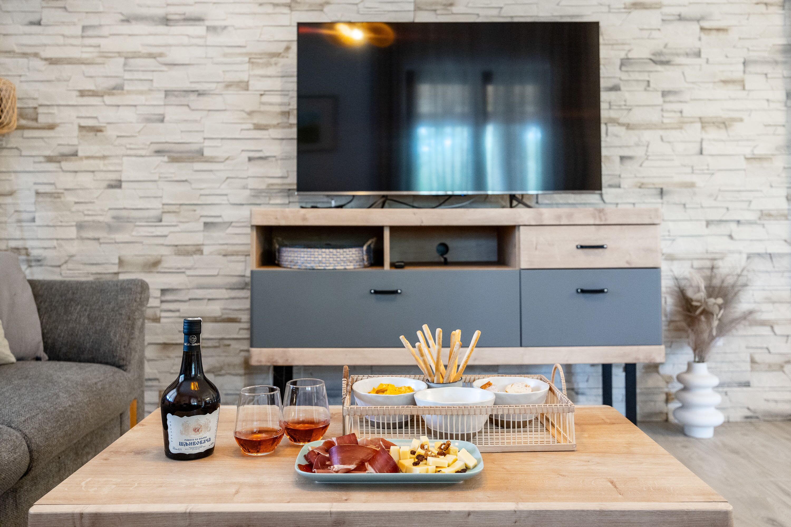 Een woonkamer met een houten salontafel, een fles wijn, glazen en een schaal met snacks.