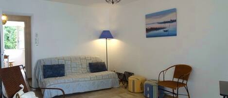 A room with a bed, two chairs, a table, a lamp, a painting, and a chandelier.