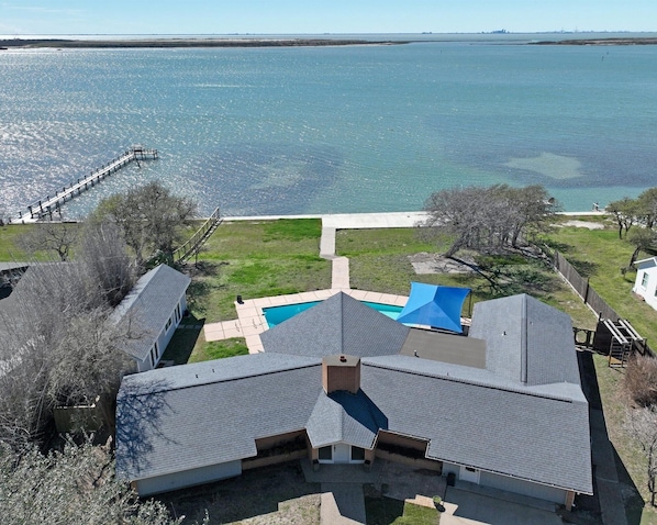 Una casa con piscina, un muelle que se adentra en el agua y un jardín con césped.