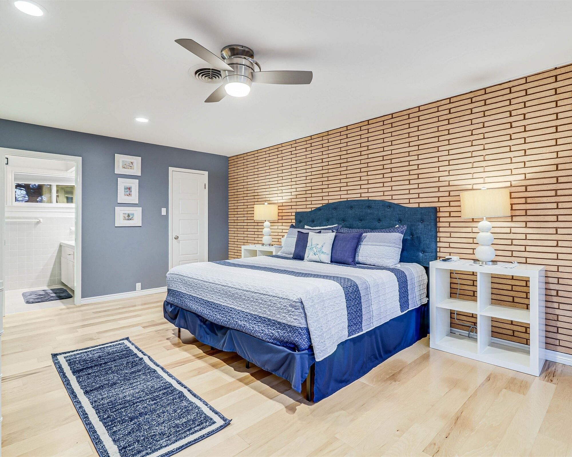 A bedroom with a bed, a nightstand, a wall-mounted lamp, a ceiling fan, and a door leading to a bathroom.