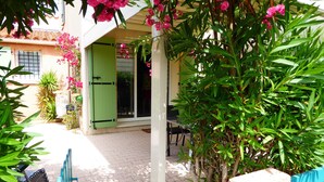 A patio area with a green door, a table, and chairs, surrounded by lush greenery and flowering plants. - Air-Conditioned Cottage with Large Terrace, Near Beach and Shops (Argelès-sur-Mer)