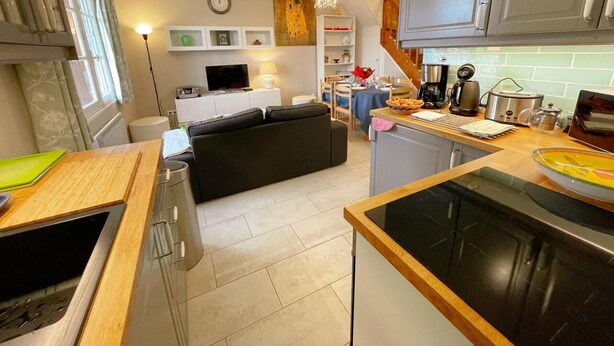 A modern kitchen with a dining area, a sofa, and a staircase leading to another level.