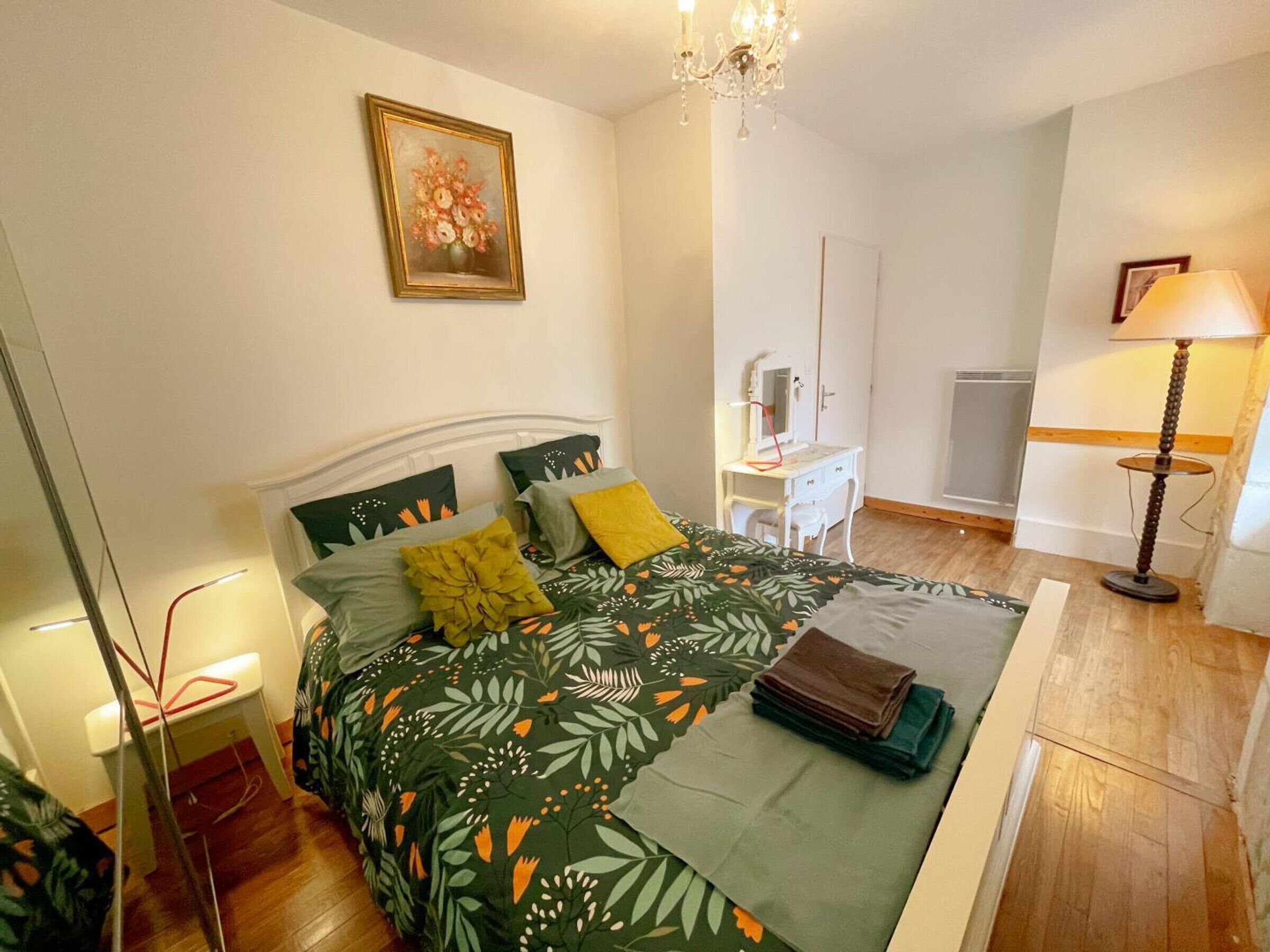 Een slaapkamer met een bed, een bureau, een stoel, een lamp en een schilderij aan de muur.
