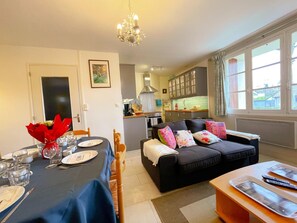 A dining area with a table set for two, a black sofa with colorful cushions, and a kitchen in the background. - Charming Historic Cottage with Garden in Richelieu, Near Loire Valley Castles (Richelieu)