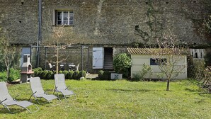 A stone building with a small garden area, including two lounge chairs and a small table.