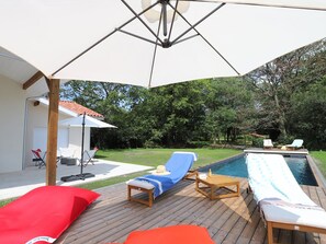 Una terraza de madera con sillas de descanso y una piscina.