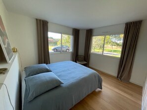 Un dormitorio con cama, una silla y ventanas amplias.