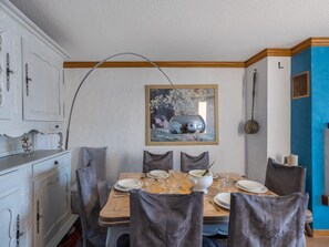 A dining area with a wooden table set for four, surrounded by grey upholstered chairs. A white cabinet with ornate details is to the left, and a blue accent wall is to the right. - Spacious Val Thorens Apartment 3 Bedrooms with Sauna and Ski-in/Ski-out Access (Val Thorens)