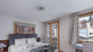 Ein Schlafzimmer mit einem großen Bett, einem Gemälde, einem Schreibtisch und einem Fenster mit Blick auf einen verschneiten Berg.