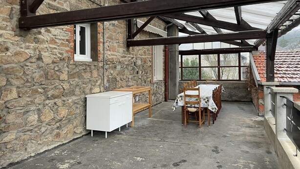 Un espace extérieur abrité, doté de murs en pierre, d’un banc en bois, d’une table avec des chaises et d’une armoire blanche.