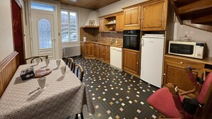 Une cuisine compacte dotée de meubles en bois, d’un réfrigérateur, d’un four à micro-ondes et d’un coin repas avec une table dressée pour deux personnes.