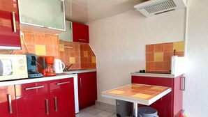 A compact kitchen with red cabinets, a small table, two stools, and a microwave. - Air-conditioned studio with balcony and parking, Cap d'Agde (Cap d'Agde naturisme)