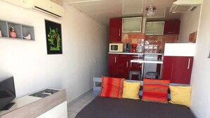 A compact room with a bed, a small desk, a TV, and a kitchenette. - Air-conditioned studio with balcony and parking, Cap d'Agde (Cap d'Agde naturisme)