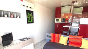 A compact living space with a sofa, a TV, a kitchenette, and a small dining area. - Air-conditioned studio with balcony and parking, Cap d'Agde (Cap d'Agde naturisme)