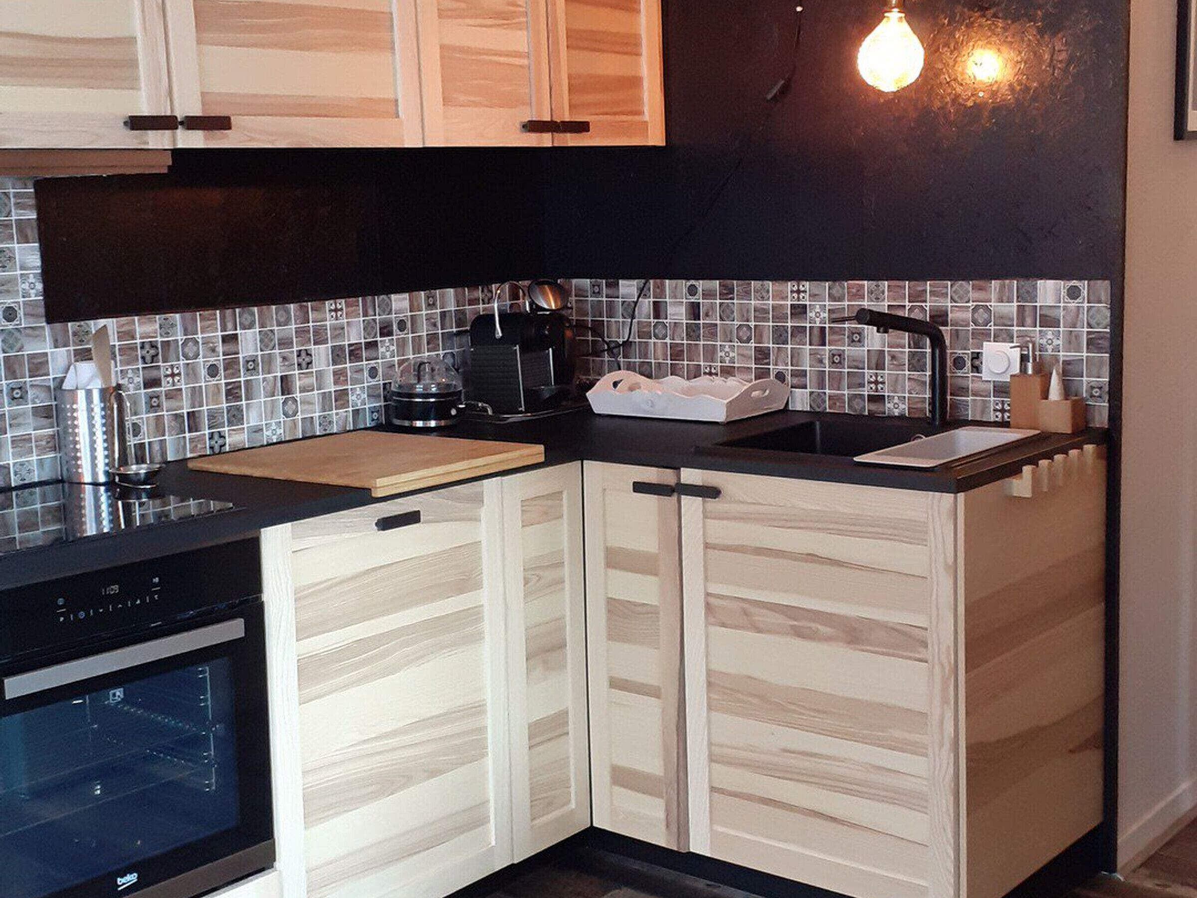 A modern kitchen with light wood cabinets, a black countertop, and a tiled backsplash.