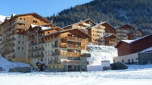 Eine Gruppe mehrstöckiger Holzhäuser mit Balkonen vor einer verschneiten Bergkulisse.