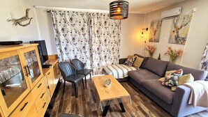 Ein Wohnzimmer mit einer Couch, zwei Sesseln, einem Couchtisch, einer Vitrine mit Glastüren und einem blumigen Vorhang.