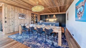 Uma área de refeições com teto de madeira, um candelabro e um tapete azul estampado.