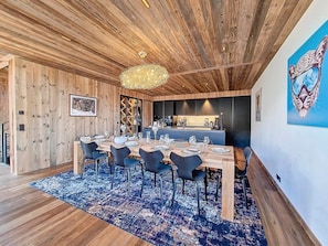 A dining area with a wooden ceiling, a chandelier, and a blue patterned rug.