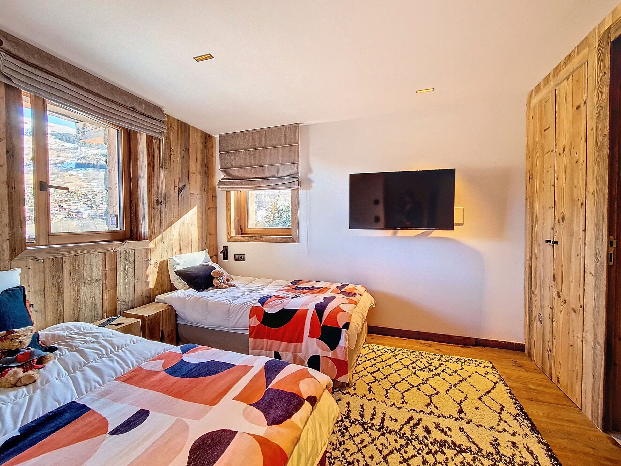 A bedroom with two beds, a TV, and a window with a view of the outdoors.