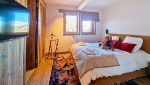 Quarto com cama, televisão, janela e piso de madeira.