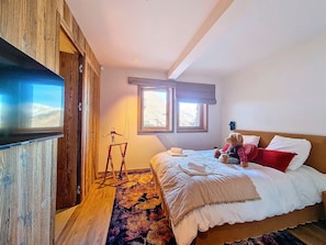 A bedroom with a bed, a television, a window, and a wooden floor.