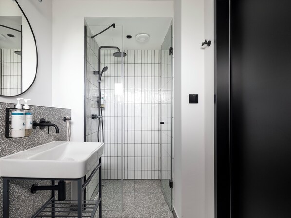 A modern bathroom with a white sink, black fixtures, and a shower area with a glass door.