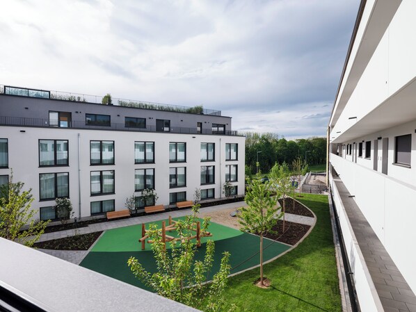 A modern building with multiple windows and balconies, a green courtyard with a playground, and a well-maintained lawn. - Numa | Munich Obersendling (Munich)