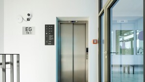 A modern elevator with a digital display, a security camera, and a sign indicating the elevator's direction.