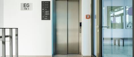 Een moderne lift met een digitaal scherm, een beveiligingscamera en een bordje dat de richting van de lift aangeeft.