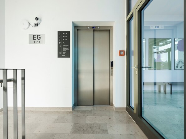 Um elevador moderno com visor digital, câmera de segurança e indicação da direção.