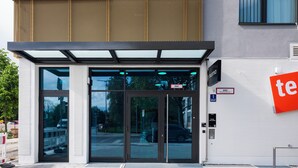 A modern building entrance with glass doors, a metal canopy, and a sign indicating 'BMW Neunkirchen Str. 1'.
