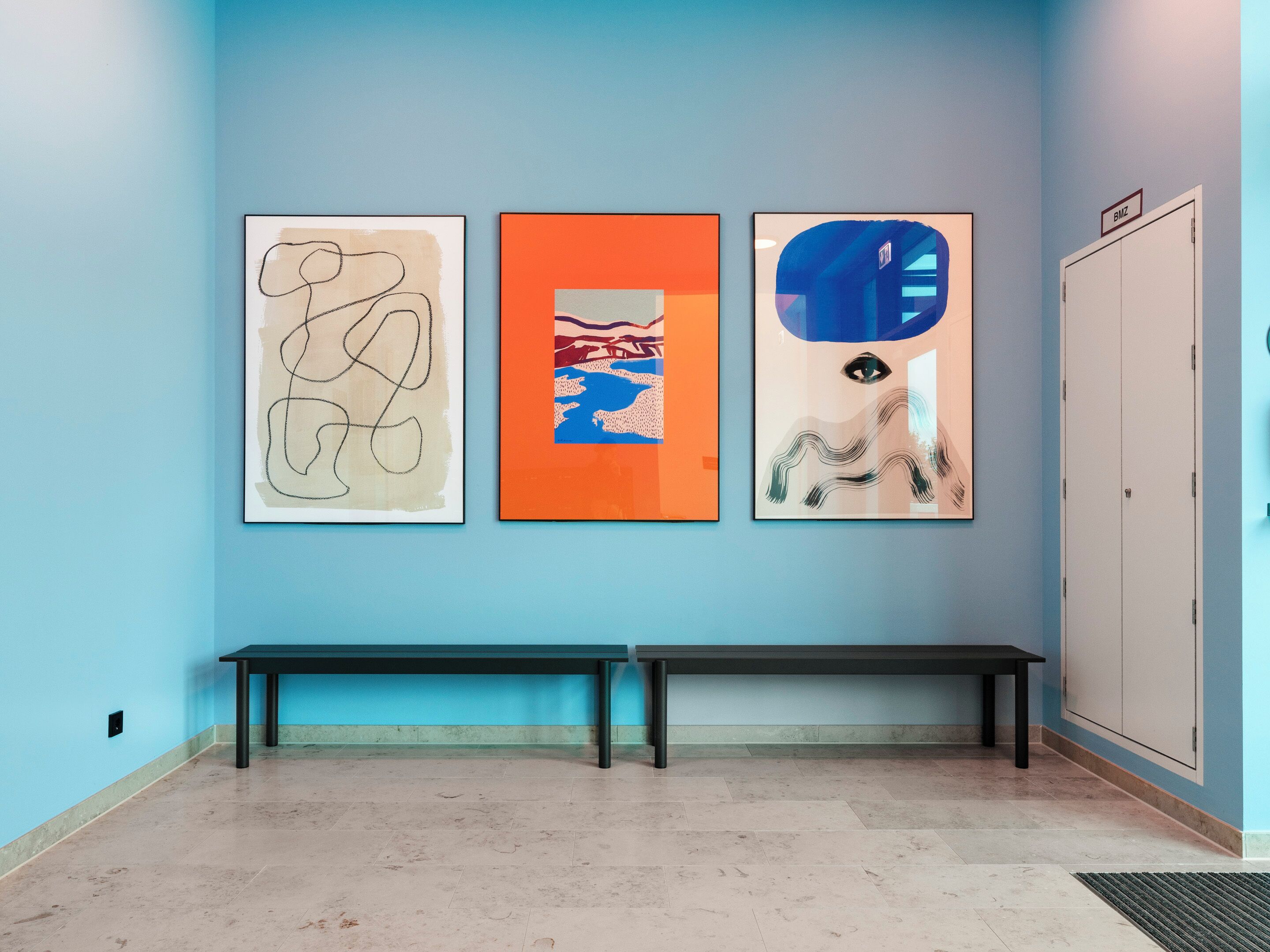 A hallway with three framed artworks on the wall, a bench, and a door labeled "BWZ".
