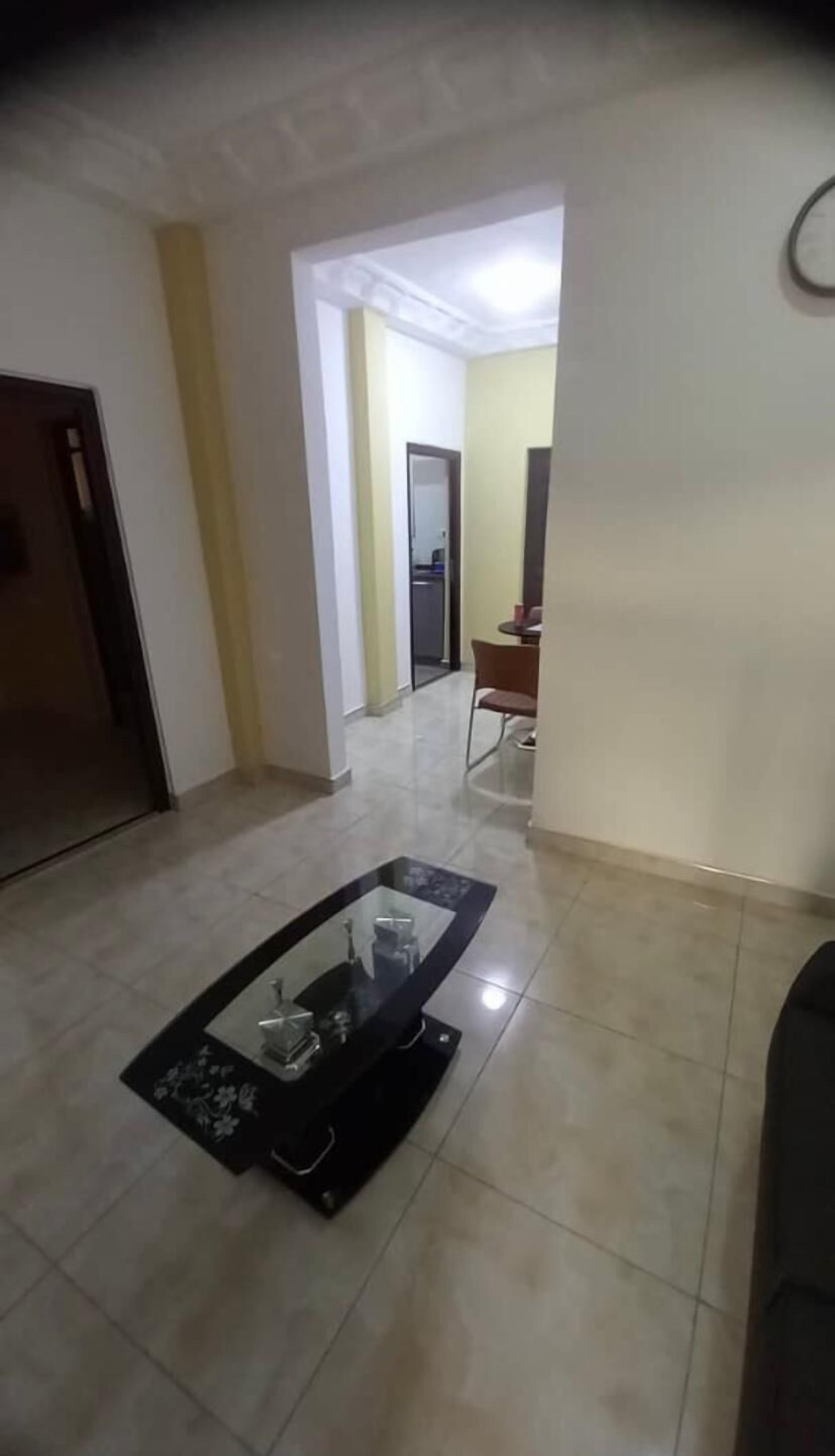 A spacious living area with a glass-top coffee table, a dining table with chairs, and a kitchen area in the background.