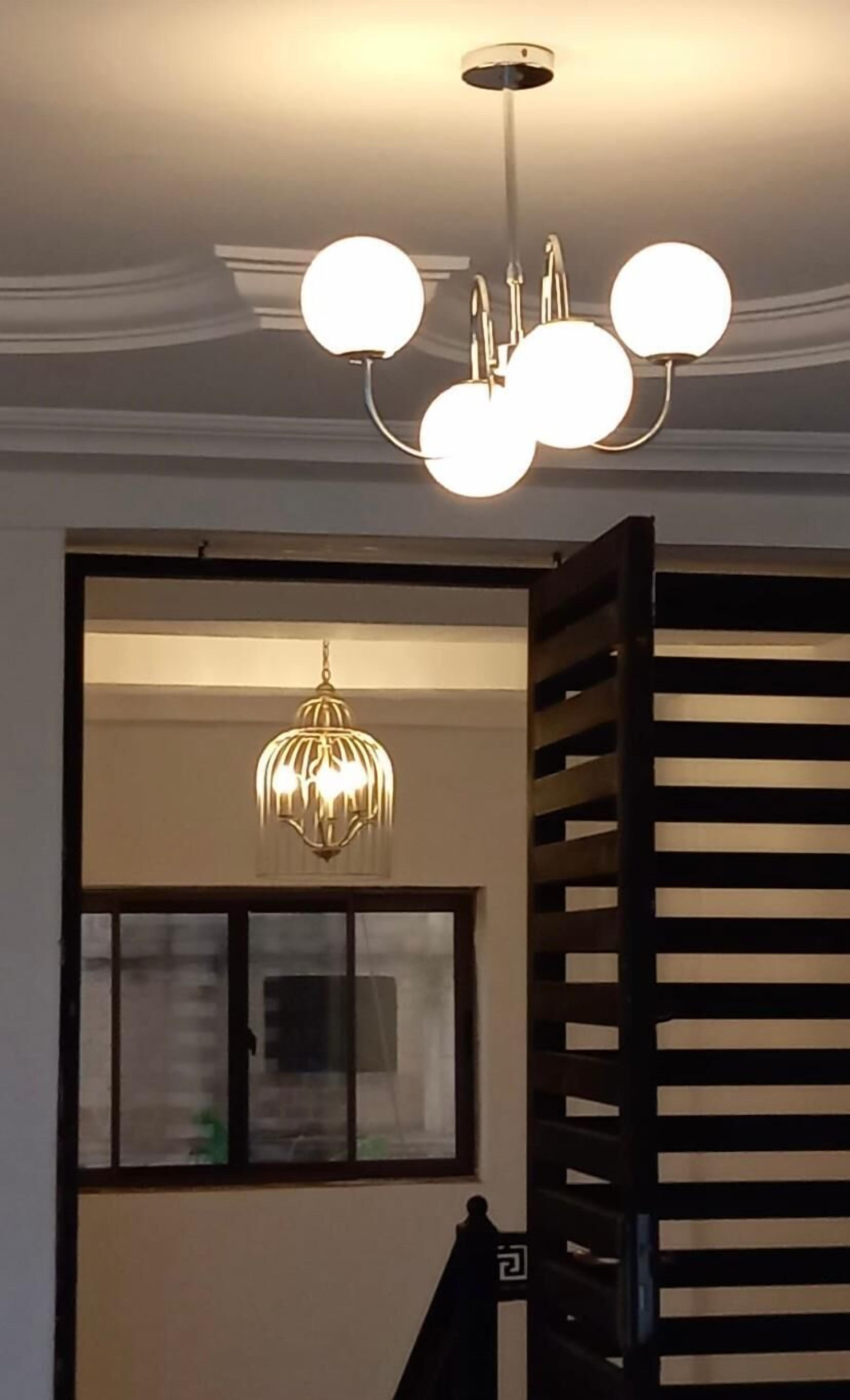 A room with a modern chandelier, a window with blinds, and a staircase with a railing.