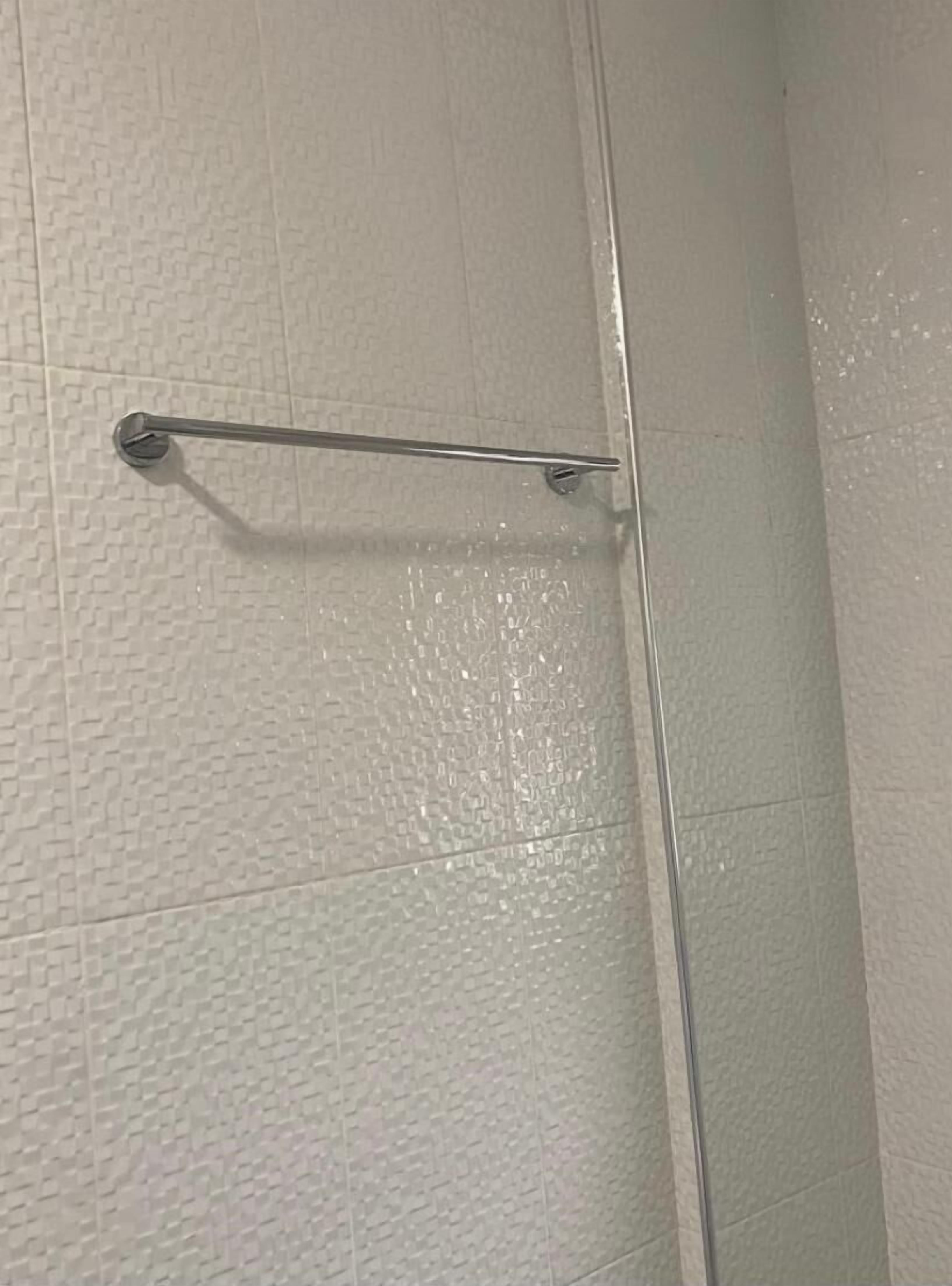 Un baño con pared blanca texturizada, un toallero de metal y una puerta de ducha transparente.