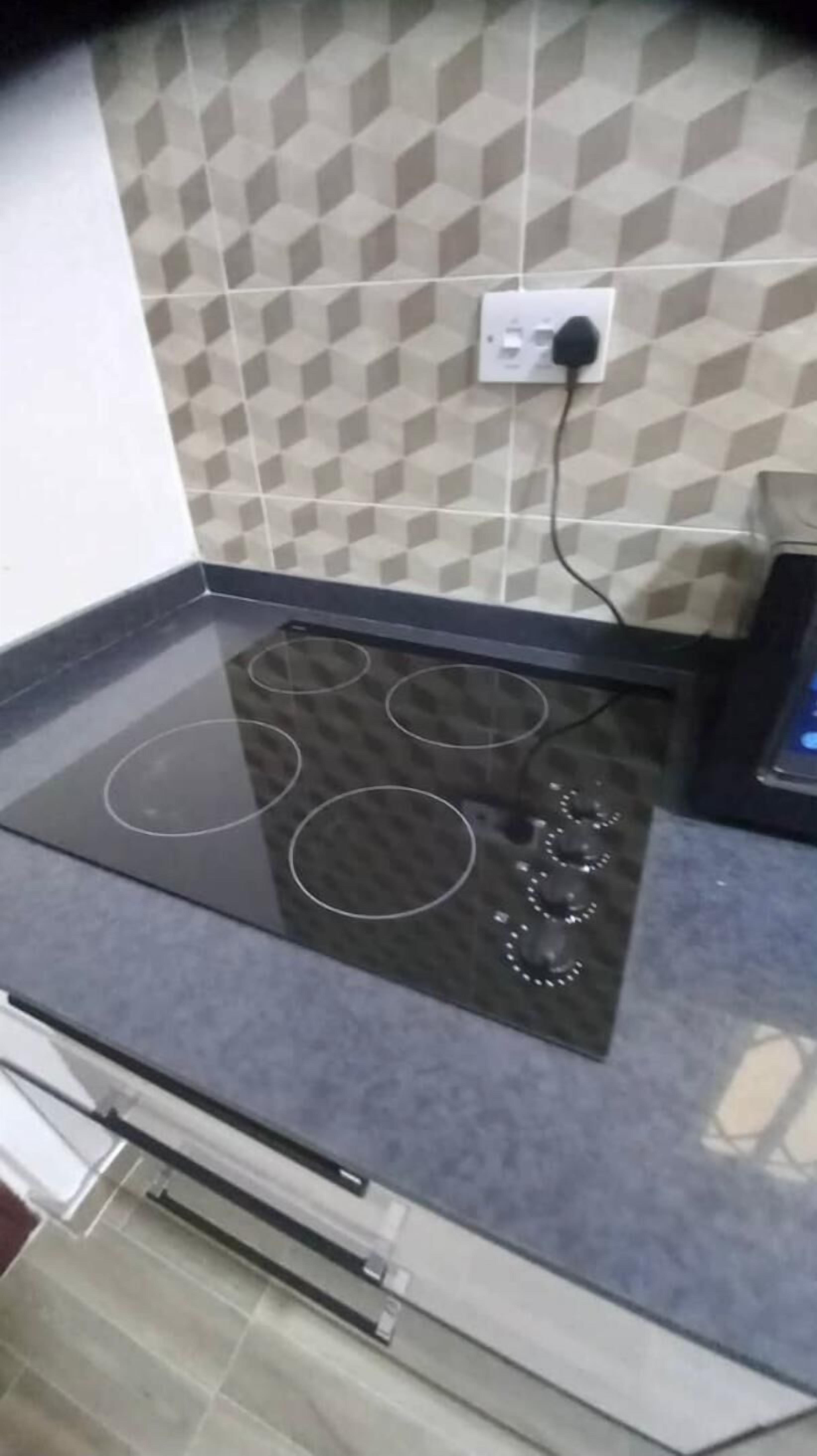 A kitchen with a black induction cooktop, a tiled backsplash, and a power outlet.
