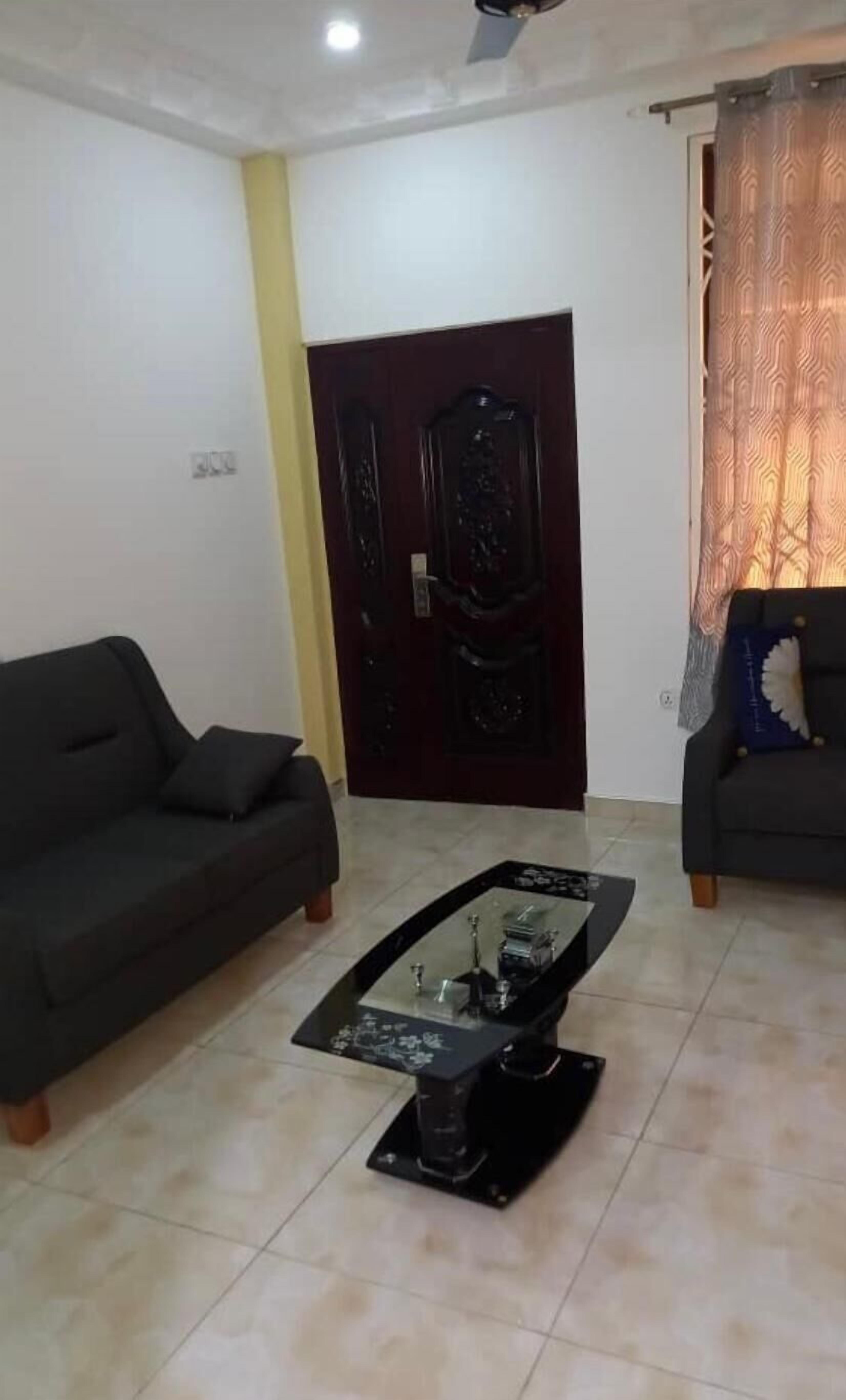 A living room with a dark-colored sofa, a glass-top coffee table with decorative items, and a dark wooden door.
