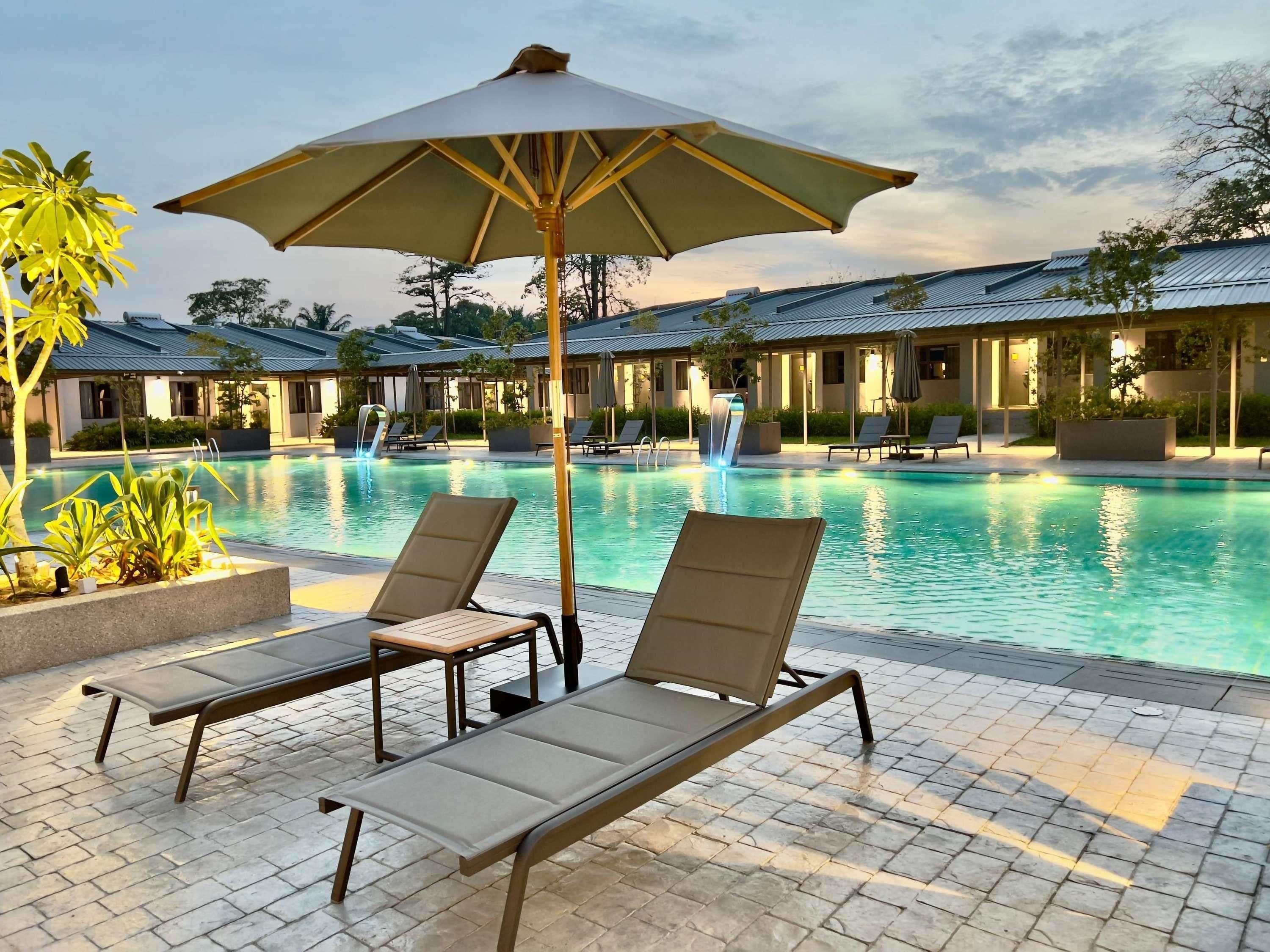 A poolside area with lounge chairs and an umbrella, surrounded by buildings with a modern design.