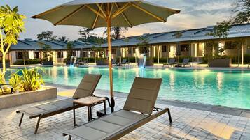 A poolside area with lounge chairs and an umbrella, surrounded by buildings with a modern design.