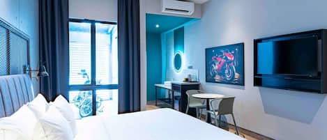 Una habitación de hotel moderna con una cama grande, un escritorio, una silla, un televisor y un aire acondicionado.
