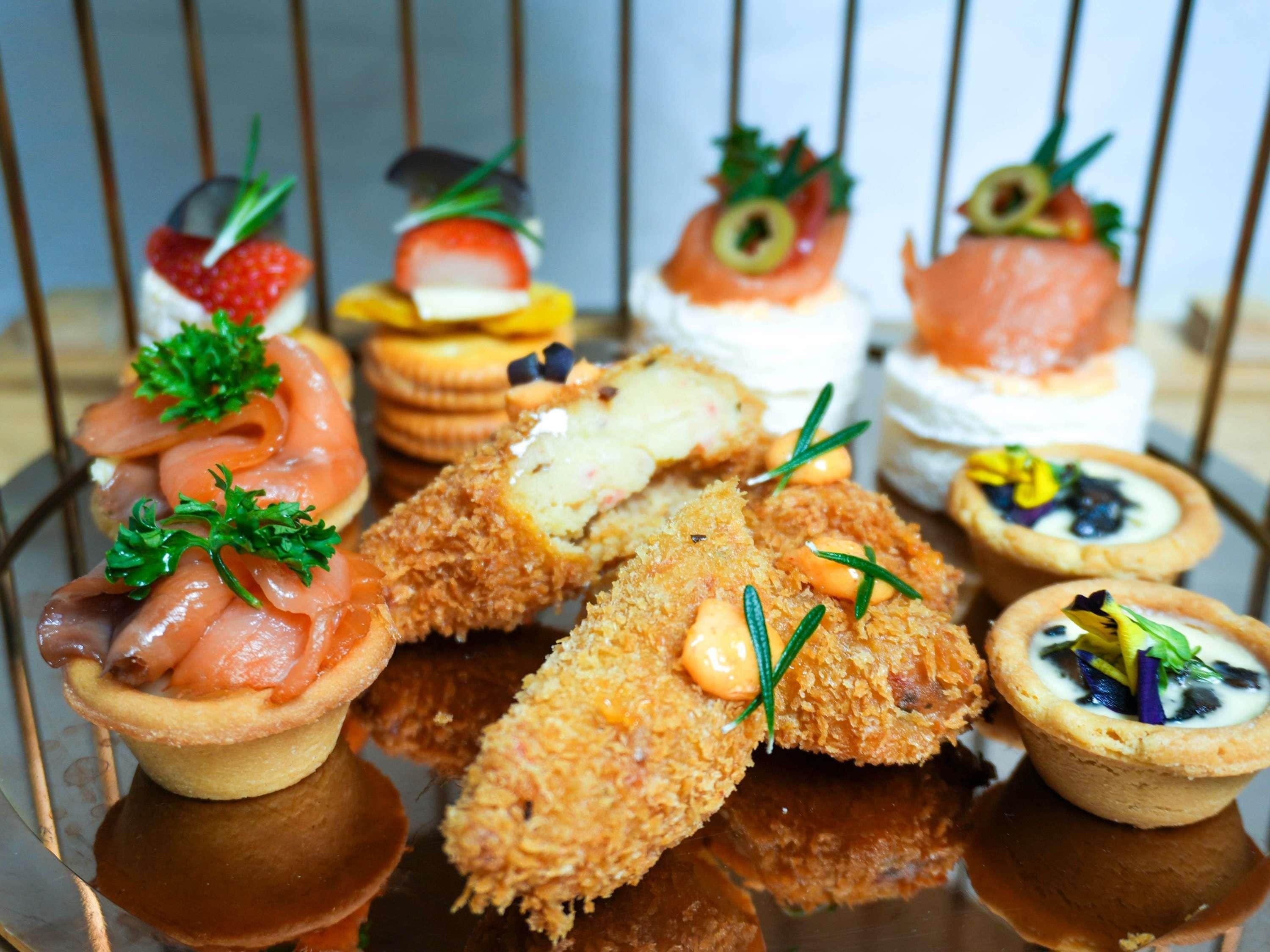 A variety of appetizers including smoked salmon, a pastry, and a tart, arranged on a reflective surface.